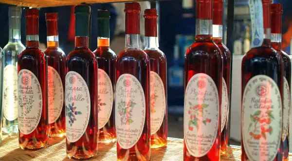 Plusieurs bouteilles de ratafia aux fruits rouges, dont le ratafia aux cerises et aux mûres, sont alignées sur une étagère en osier.