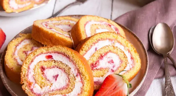 Tranches de gâteau roulé aux fraises et à la crème, parfaites pour une recette gâteau roulé facile. Une fraise coupée est posée sur l'assiette.