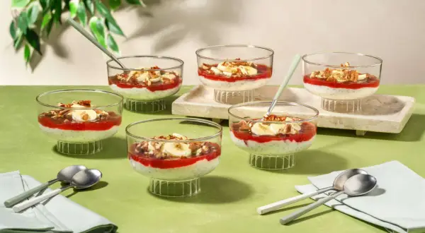 Six coupes de dessert aux graines de chia, garnies de compote de fraises, de rondelles de banane et de noix, parfaites pour un goûter.