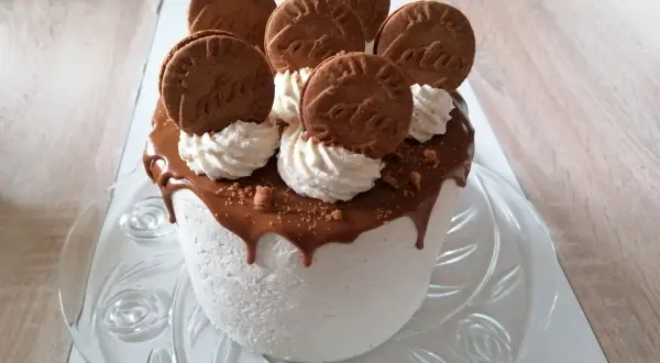 Gâteau blanc crémeux, nappé de chocolat fondant et décoré de biscuits spéculoos et de crème fouettée.