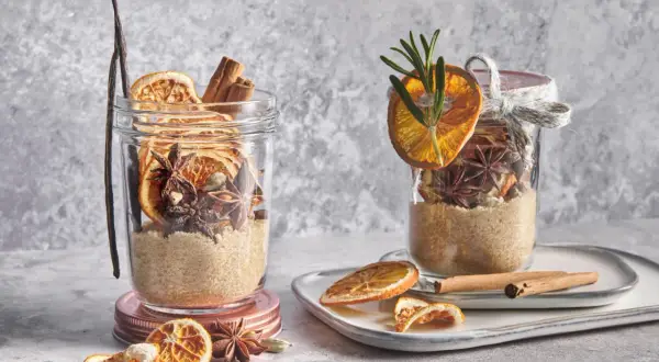 Ingrédients pour une recette de vin chaud : sucre, bâtons de cannelle, anis étoilé, cardamome, orange séchée et vanille dans des bocaux.