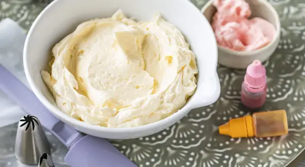 Crème au beurre à la meringue suisse onctueuse dans un bol blanc, avec des colorants et des douilles de pâtisserie.