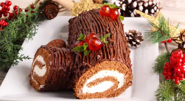 Un délicieux biscuit roulé moelleux au chocolat, décoré de cerises et de menthe, entouré de décorations de Noël.