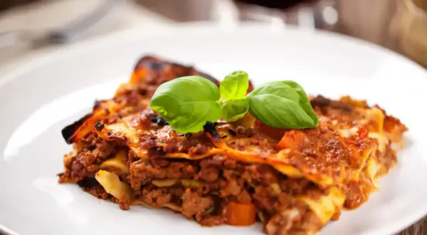 Une part de lasagne savoureuse, garnie de basilic frais, parfaite avec un verre de vin rouge.