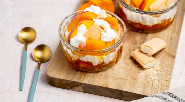 Délicieux dessert printemps : couches de fruits d'abricot, de biscuits à la cuillère et de crème fouettée dans des coupes en verre.