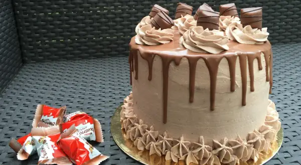 Gâteau au chocolat avec ganache Kinder Bueno, décoré de rosettes et de morceaux de chocolat.