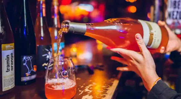 Un verre se remplit d'un vin orange pétillant, promesse d'un moment convivial. Le meilleur vin orange pour une soirée réussie.