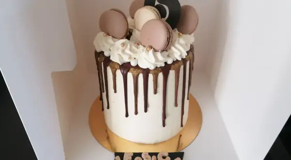 Gâteau drip cake blanc orné de macarons, de chantilly et du chiffre 15. Un délice pour les 15 ans de Jessica.