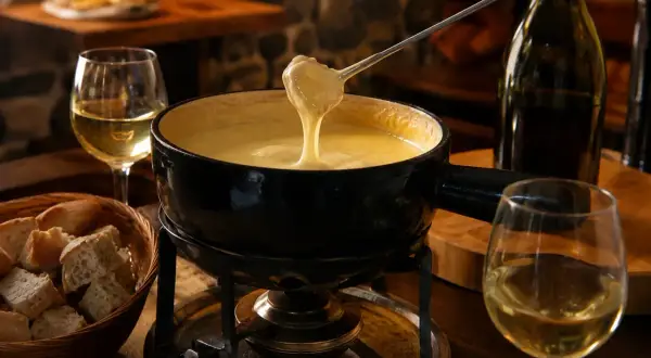 Une belle quantité de vin blanc accompagne une fondue savoyarde fumante, prête à être dégustée avec du pain croustillant.