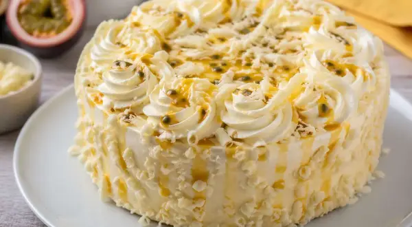 Un délicieux gâteau blanc orné de crème fouettée, de fruits de la passion et de copeaux de chocolat blanc.