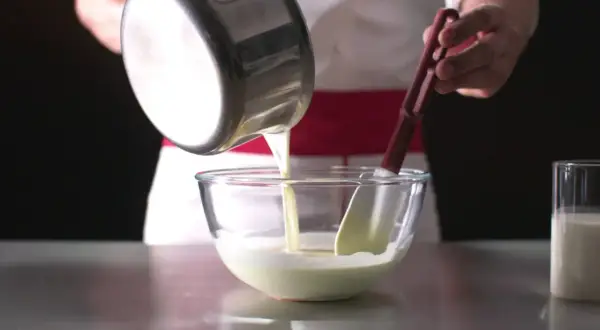 Un chef verse un liquide crémeux dans un bol, préparant une délicieuse namelaka vanille.