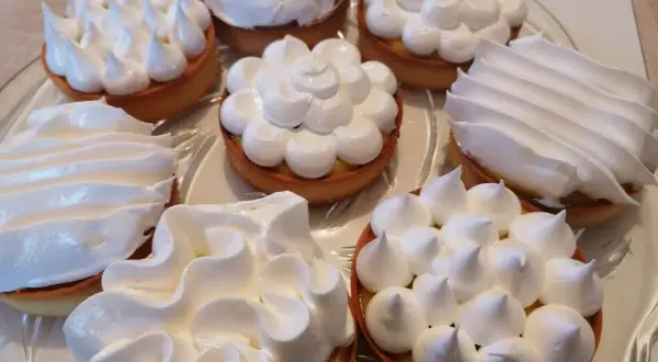 Plateau de tartelettes garnies de crème au citron et couronnées de meringue italienne, une œuvre de conservation gourmande.