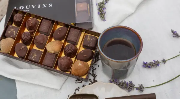 Boîte de chocolats Louvins, dont une ganache praliné, avec une tasse de café et des brins de lavande.