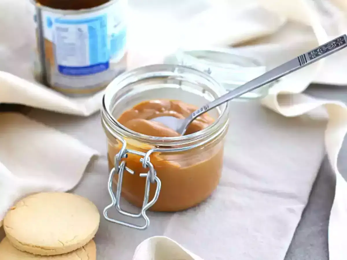 Un pot de confiture de lait onctueuse, une cuillère décorée et des biscuits sablés, prêts à être dégustés.