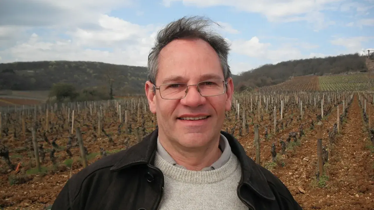 Alain Gras, souriant, se tient devant un vignoble vallonné.
