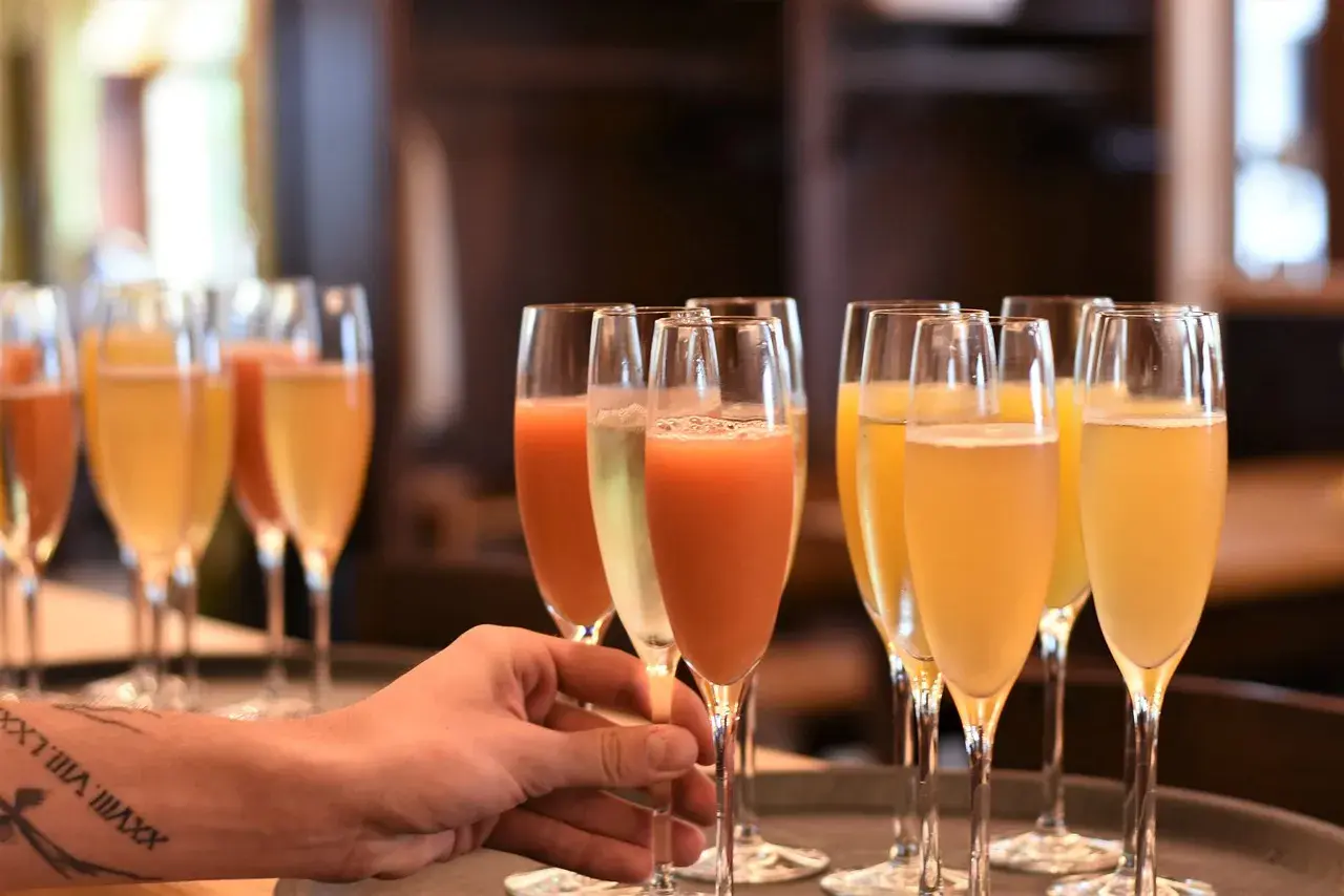 Une main saisit un verre de cocktail avec champagne, prêt à être servi. Plusieurs autres verres pétillants sont alignés.