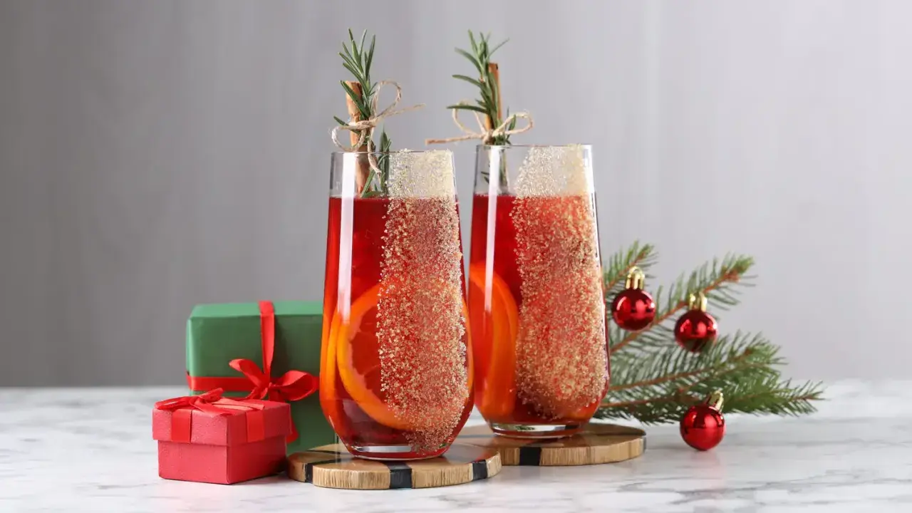 Deux verres de cocktail de Noël facile et rapide, décorés d'orange et de cannelle, avec des cadeaux et un sapin en arrière-plan.