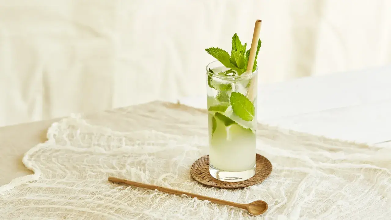 Un verre de nom de cocktail rafraîchissant avec de la menthe et de la glace, sur une nappe en dentelle.