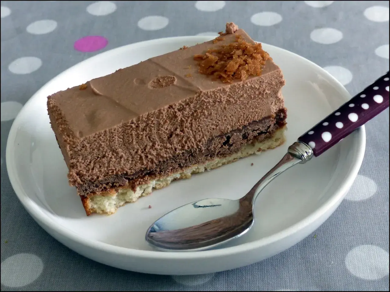 Une part de **Trianon gâteau** au chocolat, légère et aérienne, sur une assiette blanche avec une cuillère à pois.