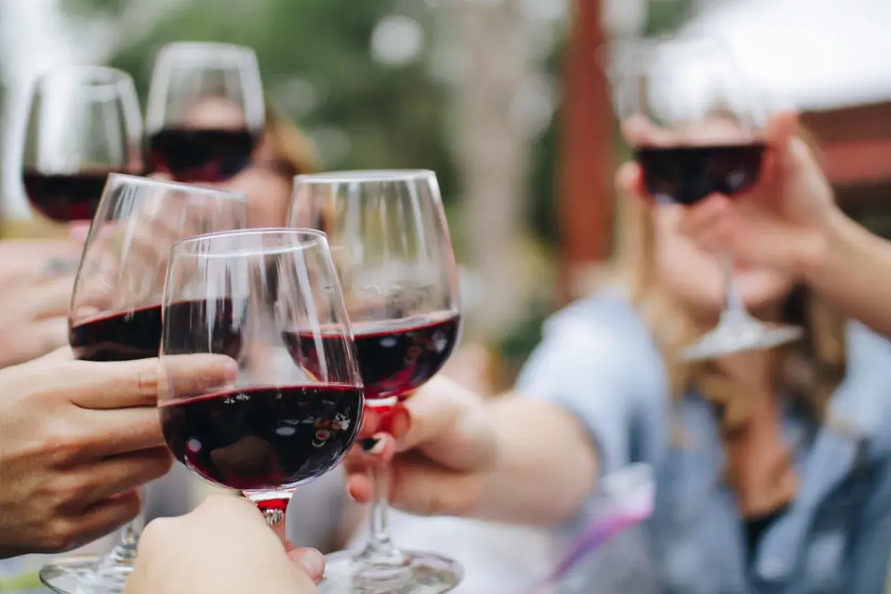 Des mains lèvent des verres de vin rouge pour un apéritif convivial.