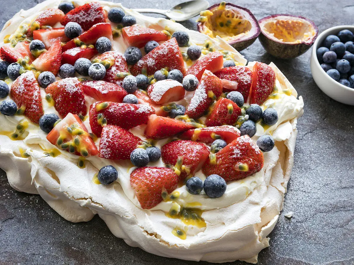 Pavlova recette : meringue aérienne garnie de crème fouettée, fraises, myrtilles et fruits de la passion. Un délice !