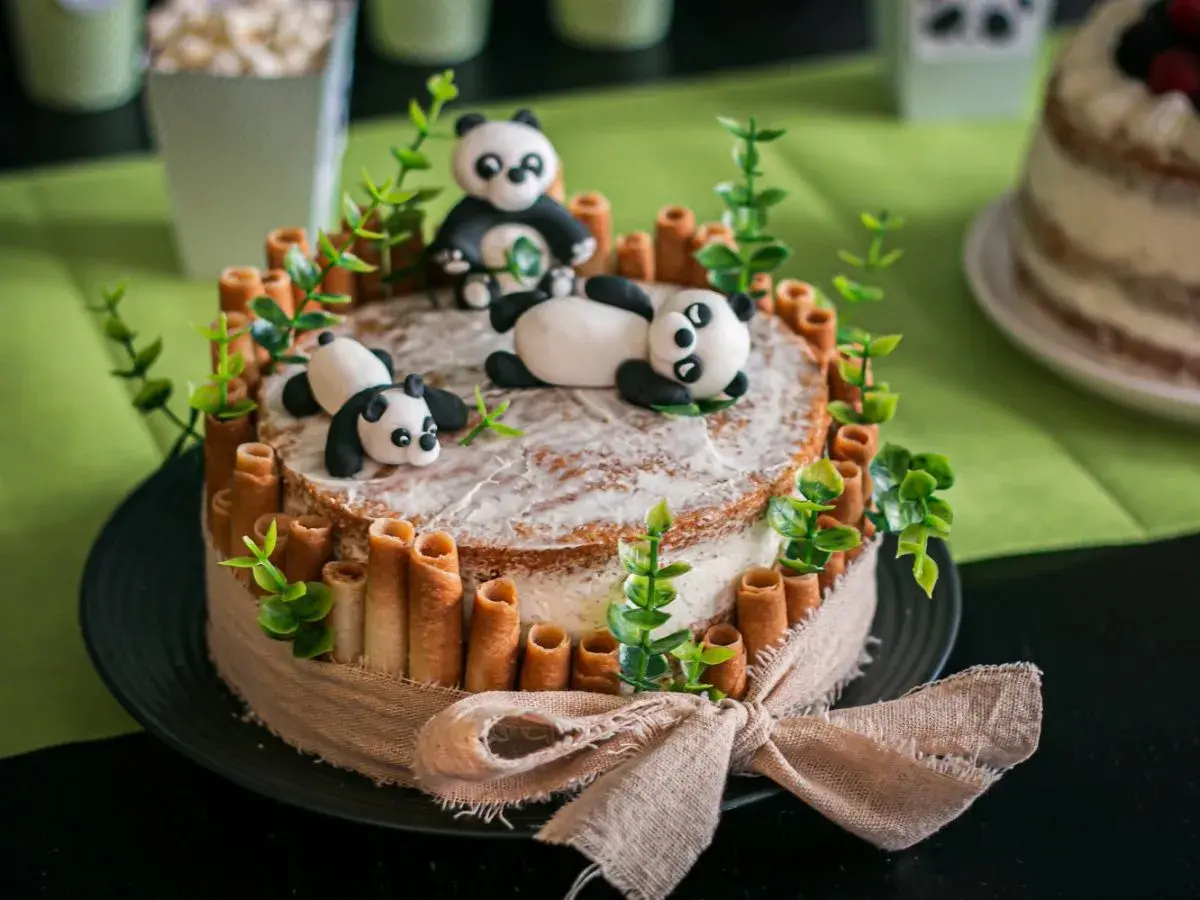 Un adorable layer cake anniversaire facile avec des pandas en pâte à sucre, des rouleaux de biscuit et des feuilles vertes.