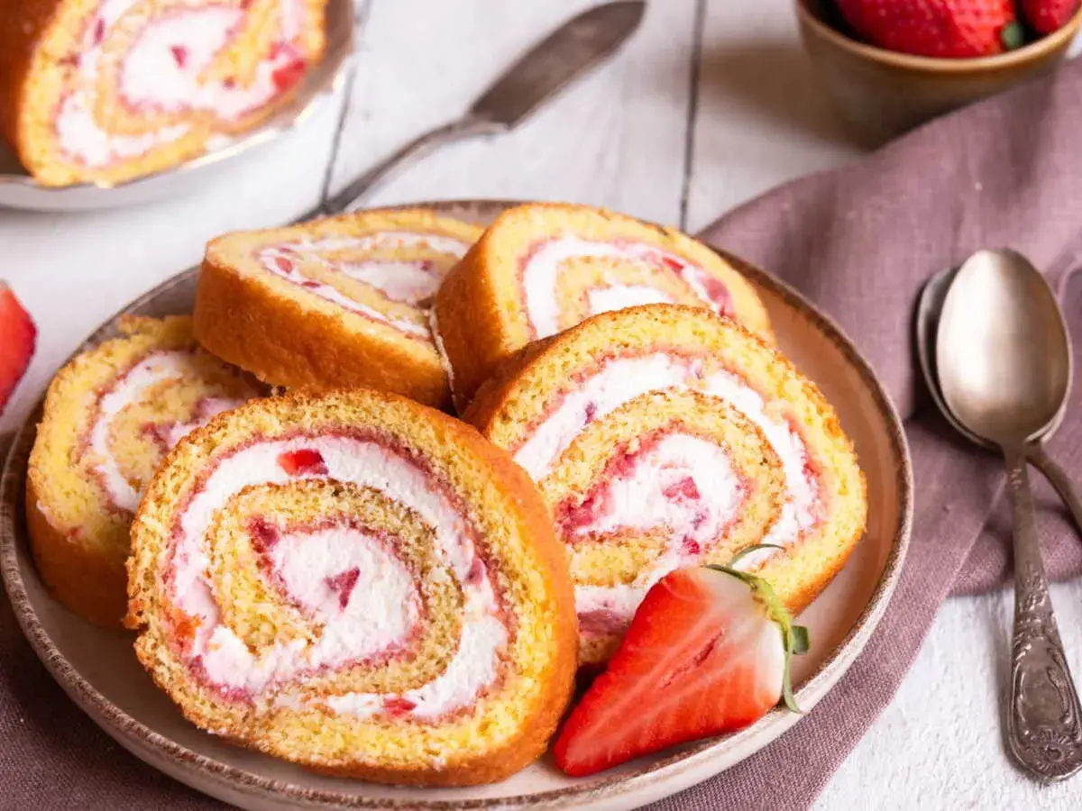 Tranches de gâteau roulé aux fraises et à la crème, parfaites pour une recette gâteau roulé facile. Une fraise coupée est posée sur l'assiette.