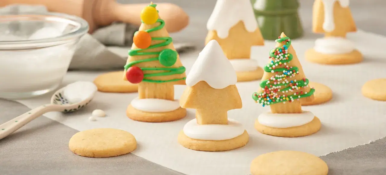 Biscuits en forme de sapins décorés de glaçage vert, vermicelles colorés et bonbons. Une recette festive à partager.