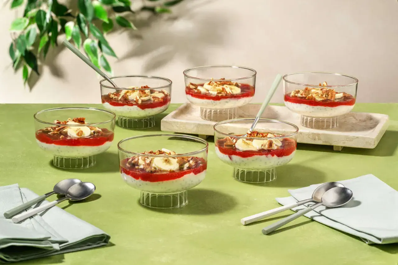 Six coupes de dessert aux graines de chia, garnies de compote de fraises, de rondelles de banane et de noix, parfaites pour un goûter.