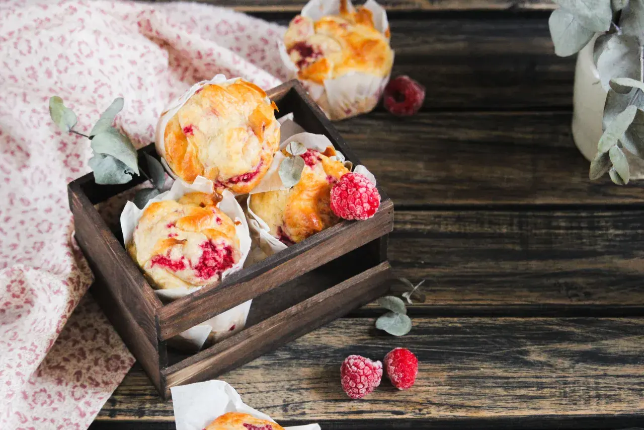 Muffins framboise dorés et moelleux dans une caisse en bois, décorés de quelques framboises fraîches.