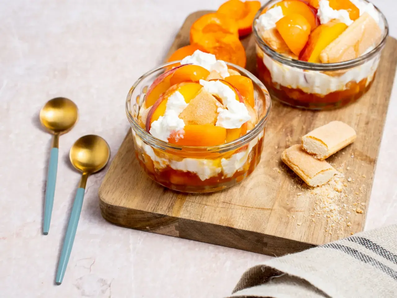 Délicieux dessert printemps : couches de fruits d'abricot, de biscuits à la cuillère et de crème fouettée dans des coupes en verre.