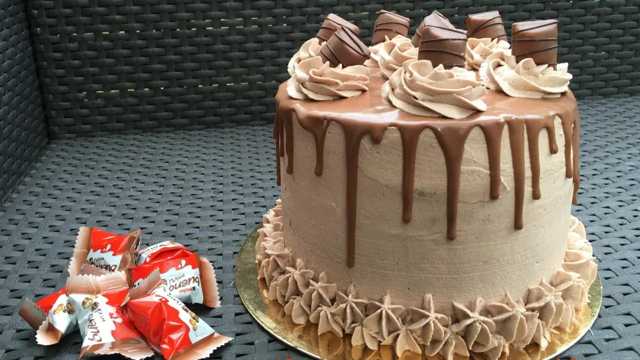 Gâteau au chocolat avec ganache Kinder Bueno, décoré de rosettes et de morceaux de chocolat.