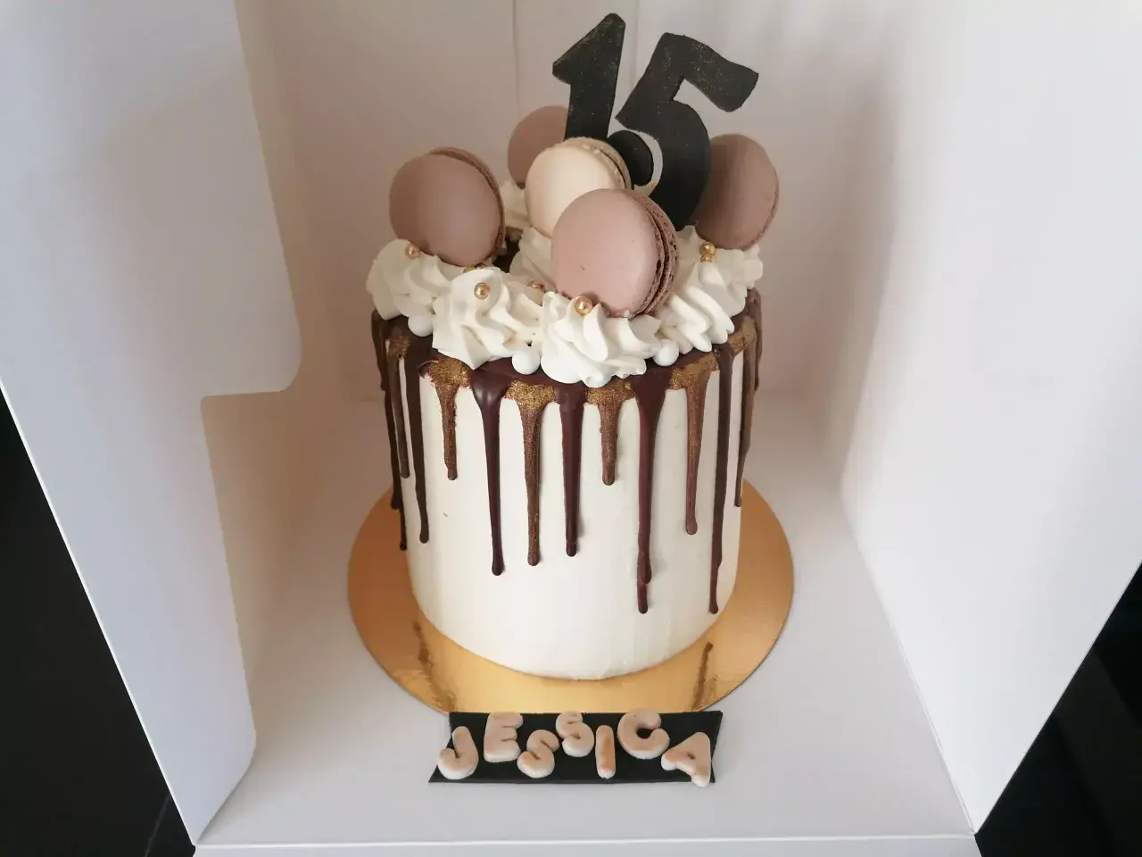 Gâteau drip cake blanc orné de macarons, de chantilly et du chiffre 15. Un délice pour les 15 ans de Jessica.