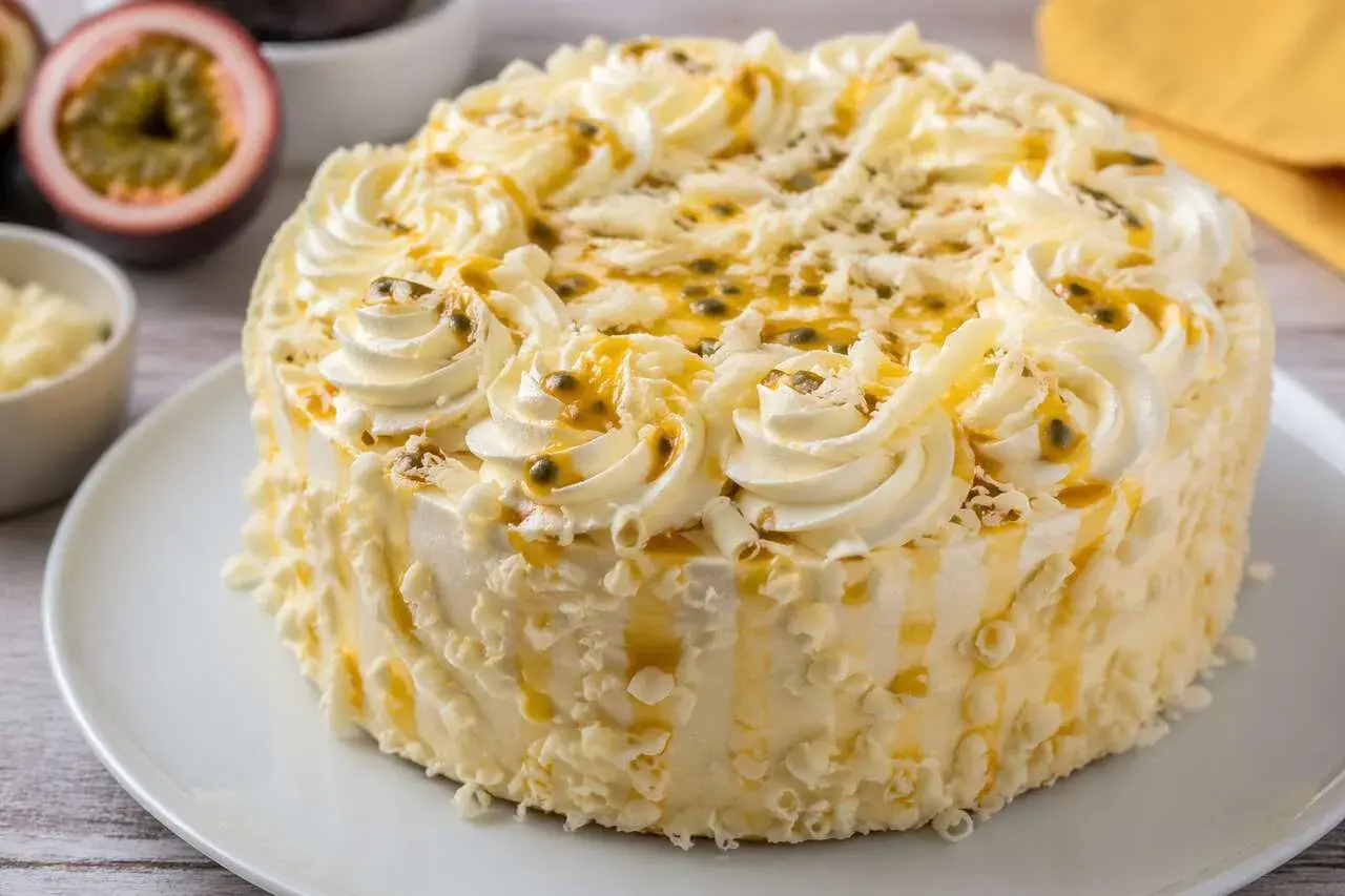Un délicieux gâteau blanc orné de crème fouettée, de fruits de la passion et de copeaux de chocolat blanc.