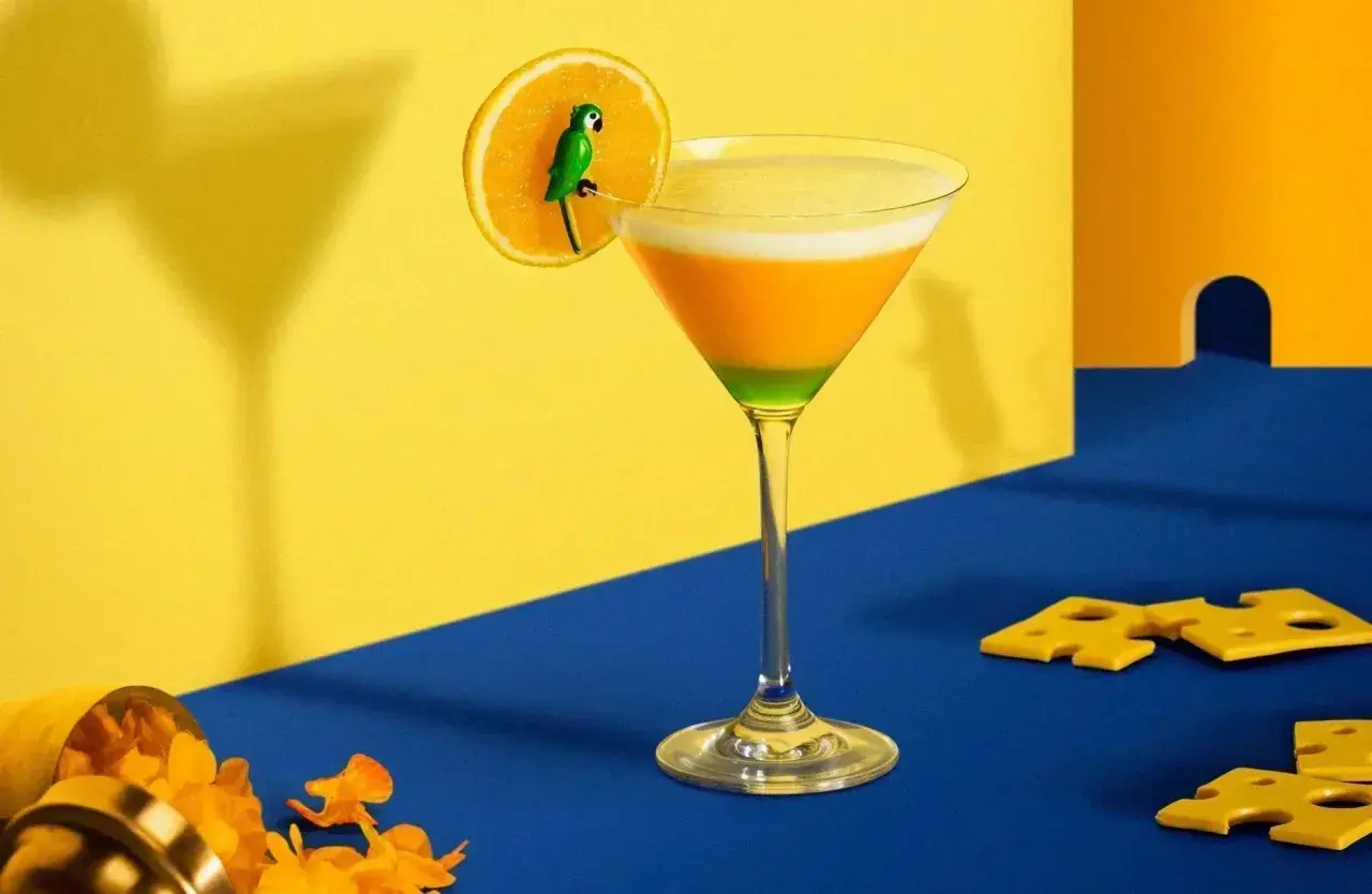 Cocktail aux couches orange et verte, garni d'une tranche d'orange avec un petit perroquet. Un exemple d'inspiration pour des noms de cocktails originaux.