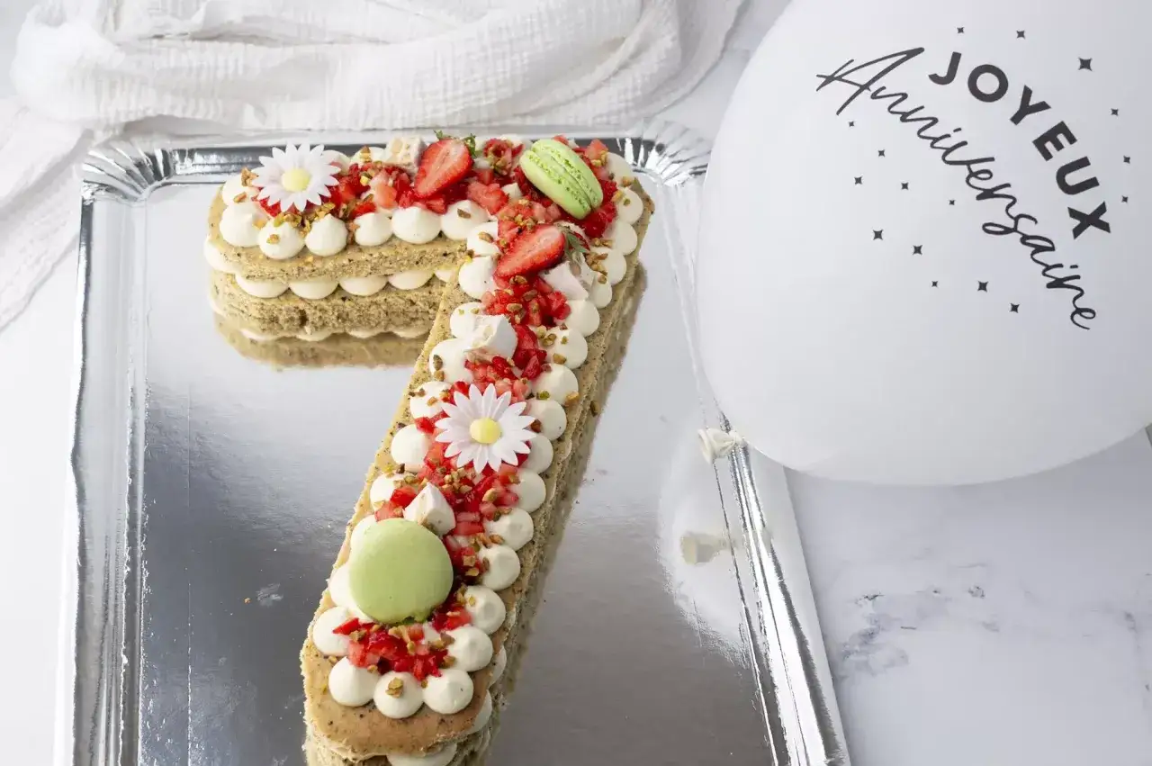 Un délicieux number cake pistache, garni de fraises, macarons et fleurs en sucre, prêt pour un joyeux anniversaire.