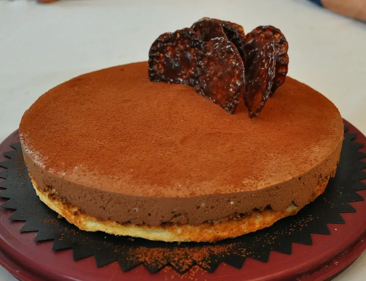 Un délicieux trianon gâteau au chocolat, saupoudré de cacao et orné de tuiles croustillantes.