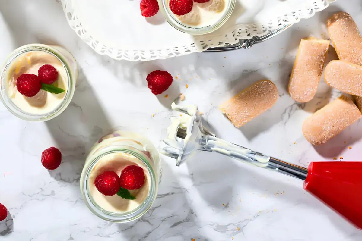 Des verrines de tiramisu aux framboises, garnies de chantilly maison, avec des biscuits à la cuillère et un mixeur plongeant.