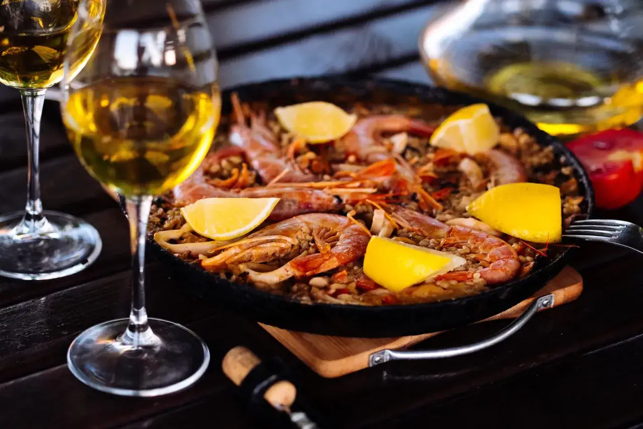 Paella aux crevettes et citrons, accompagnée de deux verres de vin blanc. Un accord parfait pour savoir quel vin avec une paella.