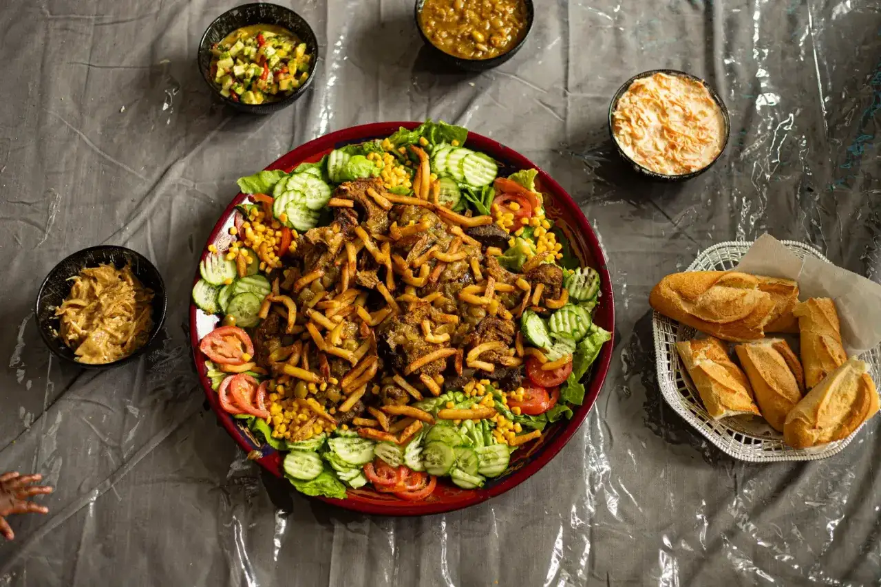 Un plat généreux de type de viande rouge, garni de frites croustillantes, servi avec salade, maïs, tomates, concombres et pains.