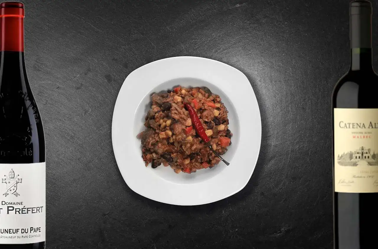 Plat de chili con carne épicé avec une touche de piment rouge, accompagné de deux bouteilles de vin rouge. Quel vin avec chili con carne ?