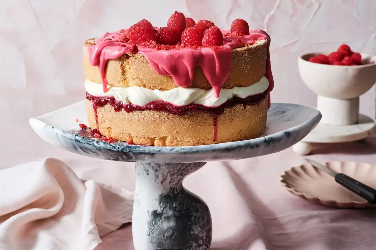Un délicieux victoria sponge cake, garni de crème, de confiture de framboises et de framboises fraîches, avec un glaçage rose dégoulinant.