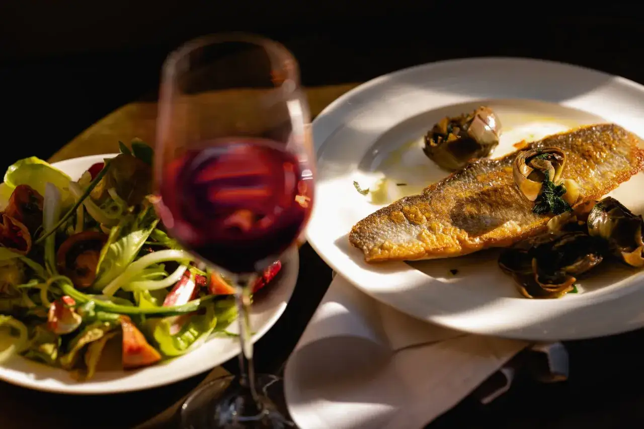 Un verre de vin rouge accompagne un délicieux poisson grillé et une salade fraîche.