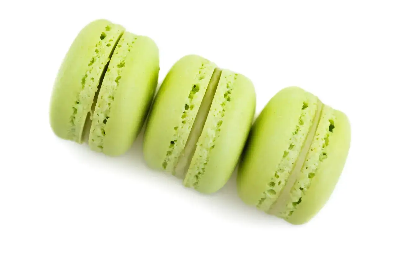 Trois macarons verts vifs, garniture à la ganache pistache, sur fond blanc.