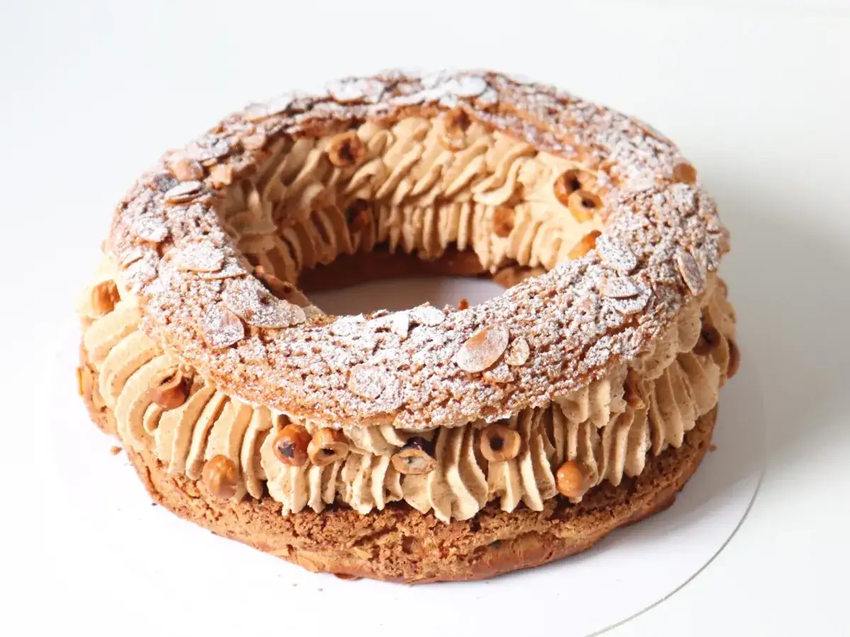 Un Paris-Brest rond, garni de crème pralinée et parsemé d'amandes effilées et de noisettes.