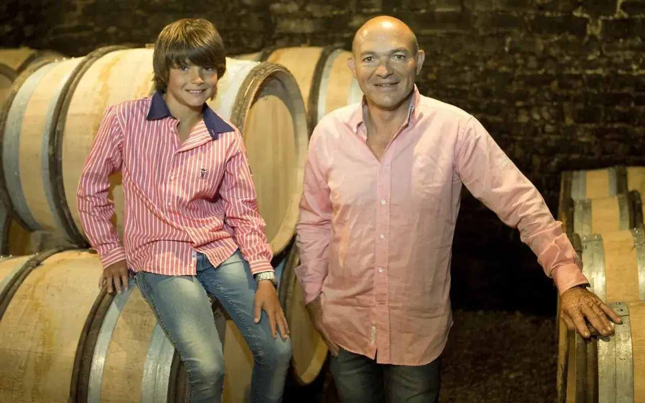 Alain Gras et son fils posent devant des tonneaux de vin dans une cave.