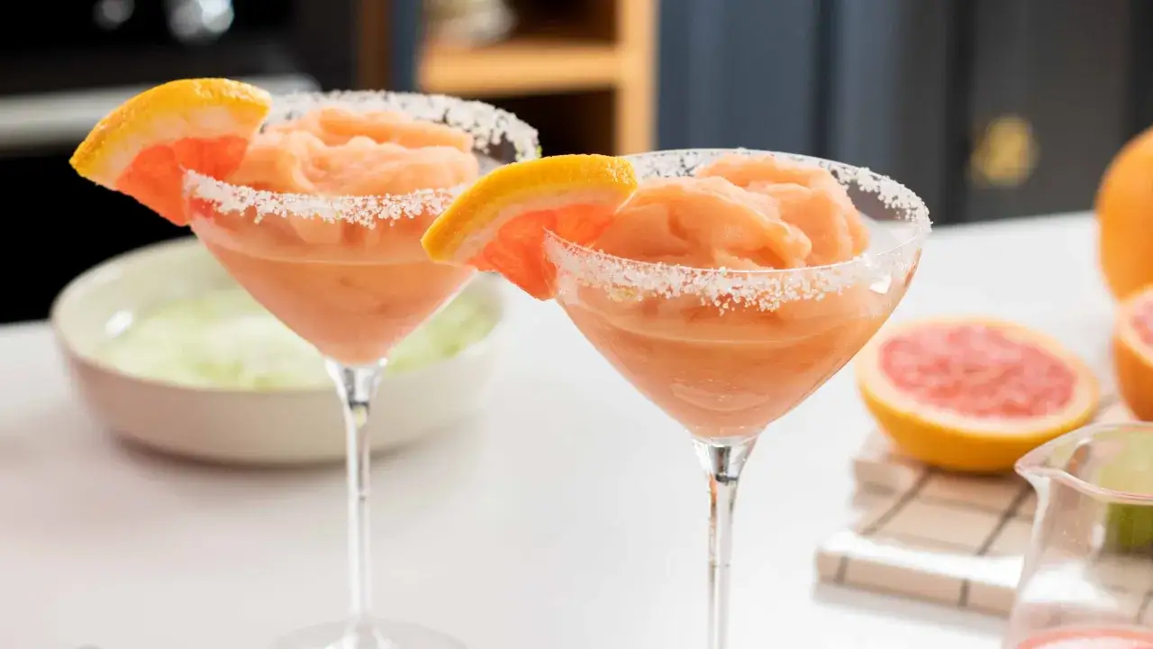 Deux verres de cocktail estival glacé au pamplemousse, bordés de sucre et garnis d'une tranche de fruit.