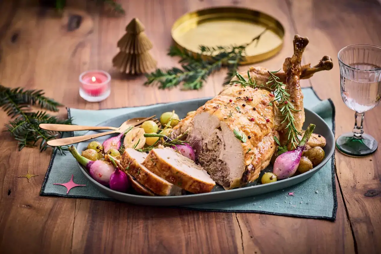 Un festin de Noël : un chapon farci doré, accompagné de petits oignons rouges, de raisins et de pommes de terre rôties. Un plat parfait pour un vin de fête.