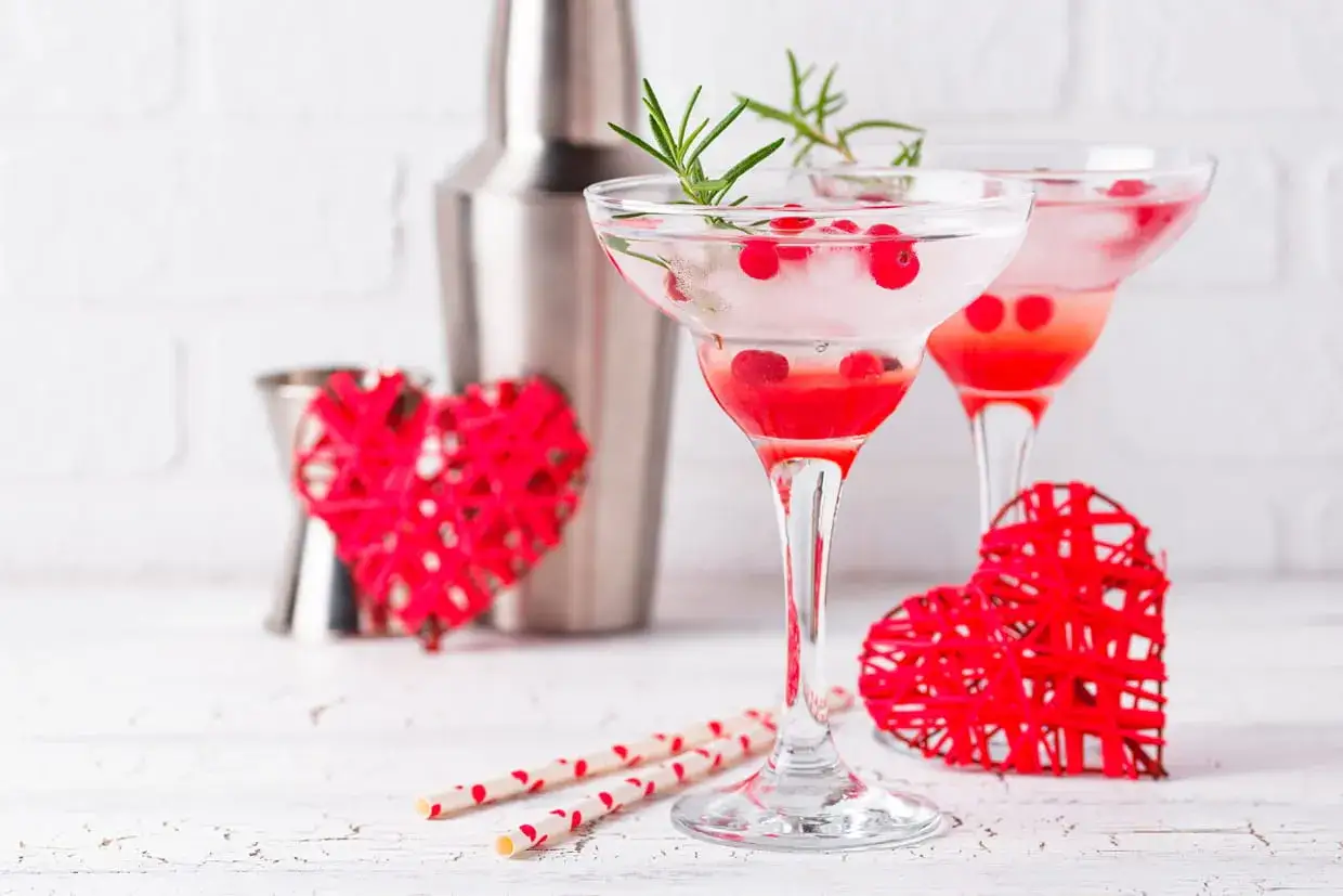 Deux cocktails sans alcool Saint-Valentin, décorés de baies rouges et de romarin, avec des cœurs rouges et des pailles festives.