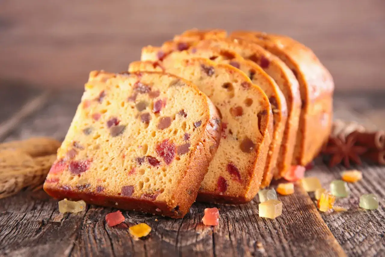 Tranches de gâteau de voyage aux fruits confits, parsemées de bonbons colorés sur fond de bois.